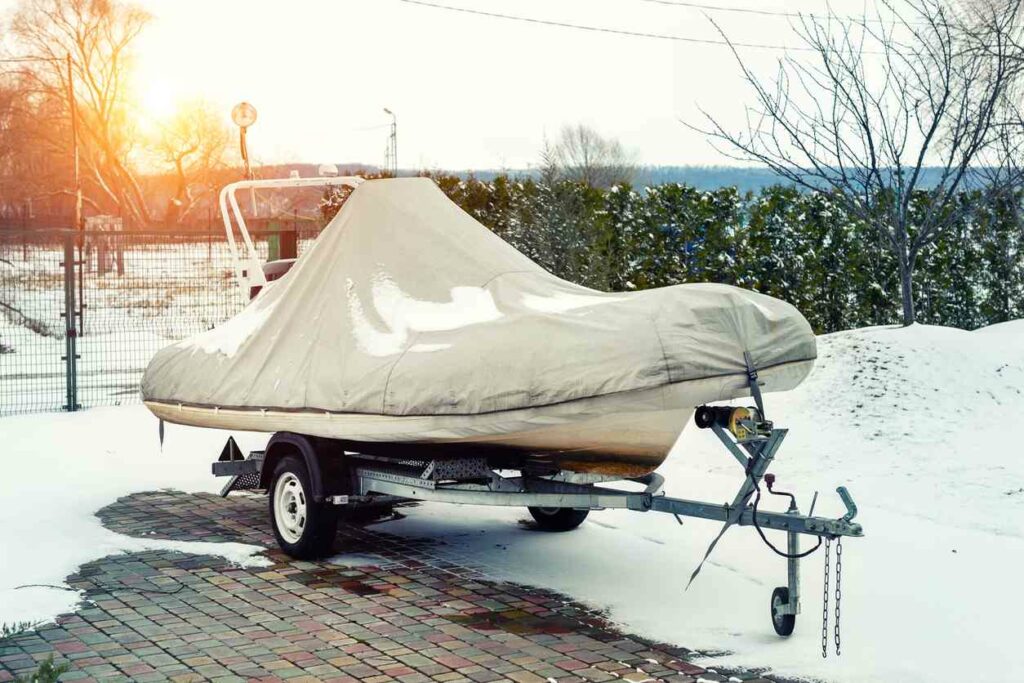 A boat on a trailer covered by a tarp, surrounded by snow