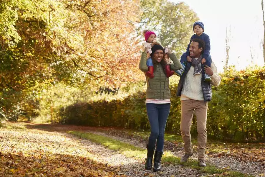 Parents hold toddlers on shoulders while standing outside in a wooded area