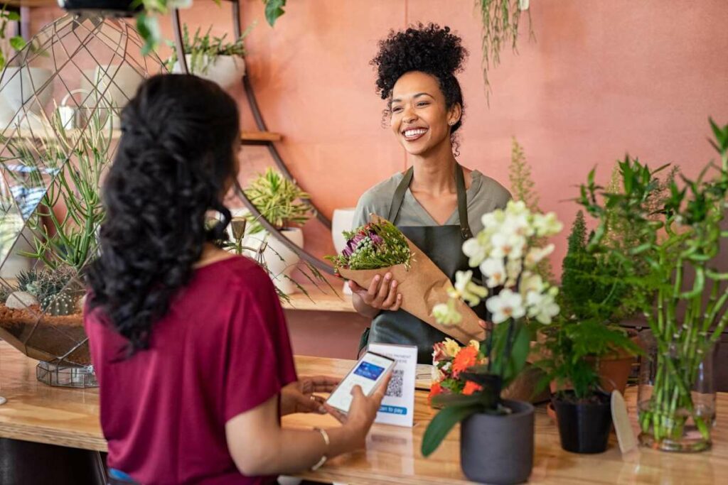 Friendly florist smiles while holding a bouquet and helping a customer