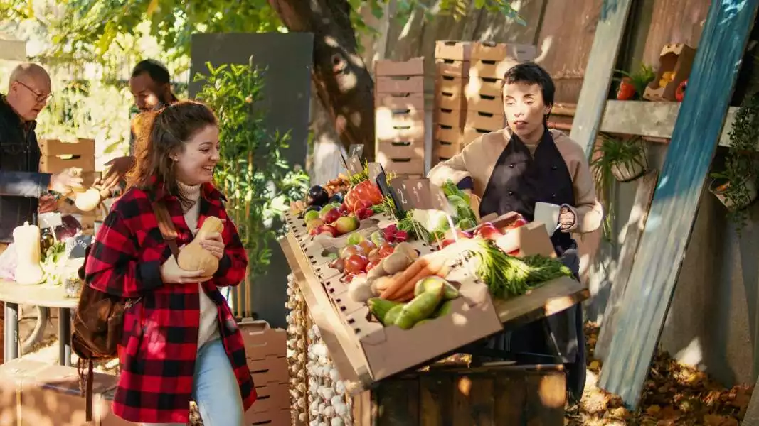 Woman buys squash from merchant selling vegetables at a farmers market