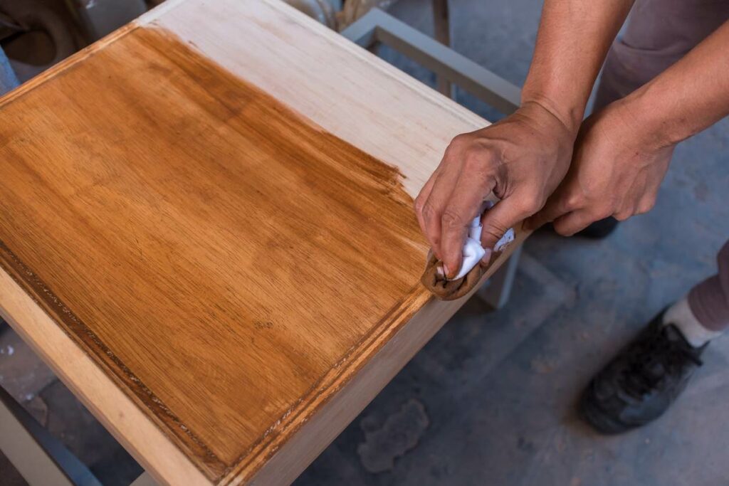 A man using a white rag to stain an unfinished oak cabinet with a darker color