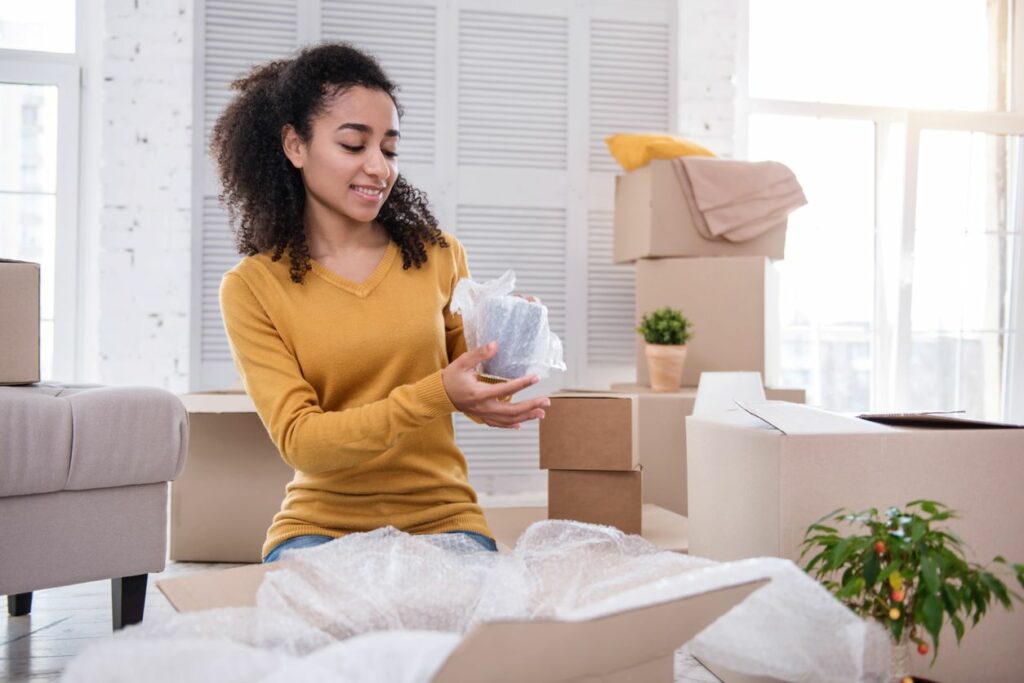 A woman securely wrapping a tea cup before placing in a storage box.