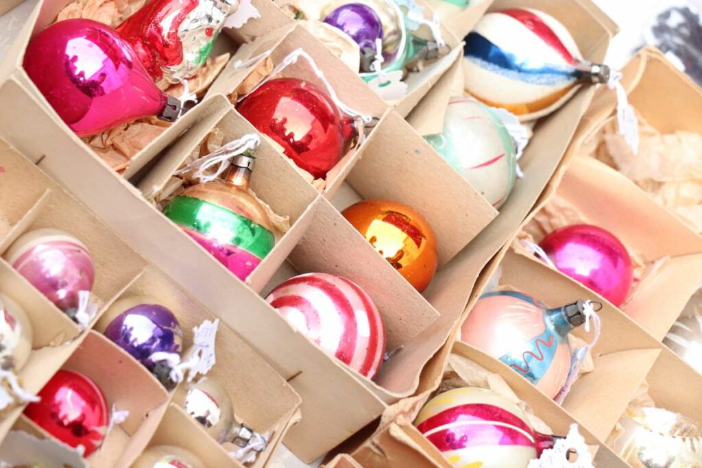 Colorful Christmas ornaments are stored in a cardboard box with protective dividers.
