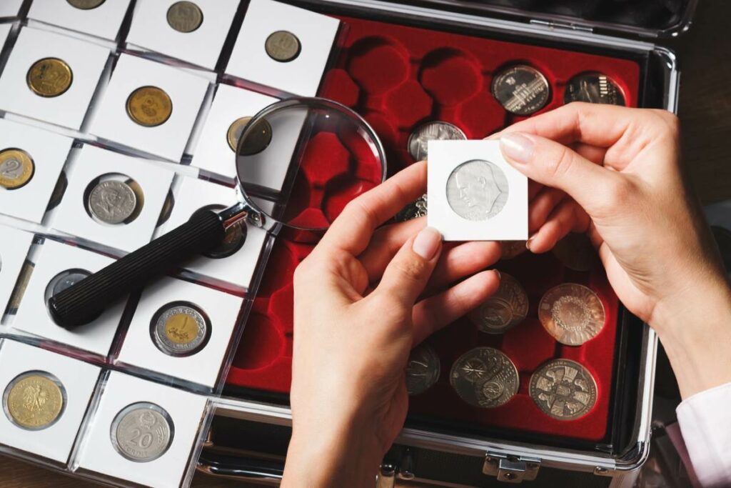 A person examines a box filled with cells of collectible coins, which includes a magnifying glass. 