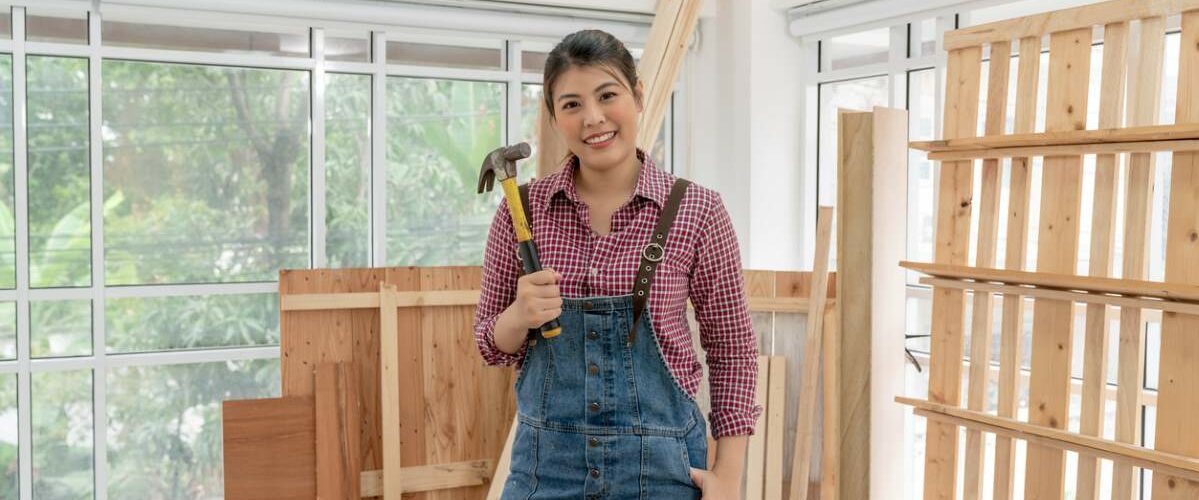 A young woman smiles as she stands in her woodworking workshop.