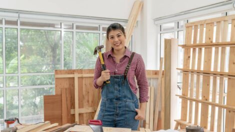 A young woman smiles as she stands in her woodworking workshop.