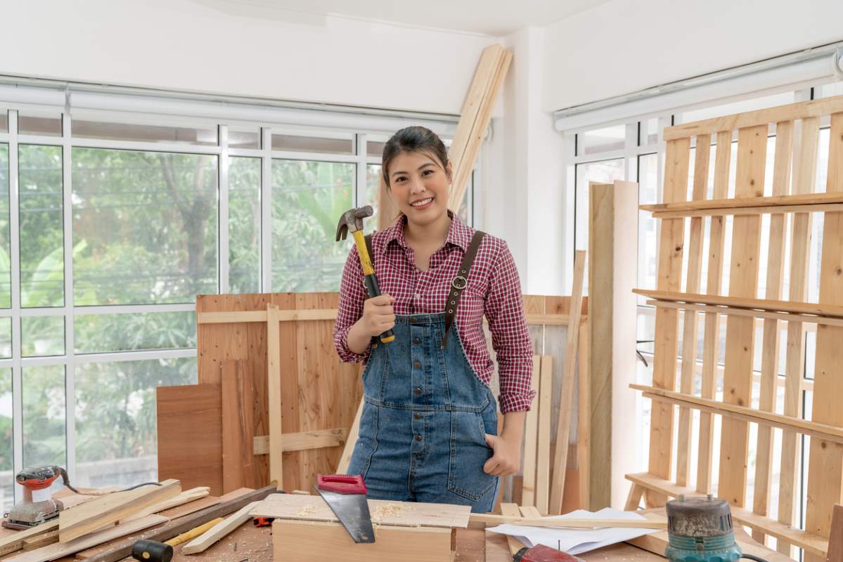 A young woman smiles as she stands in her woodworking workshop.