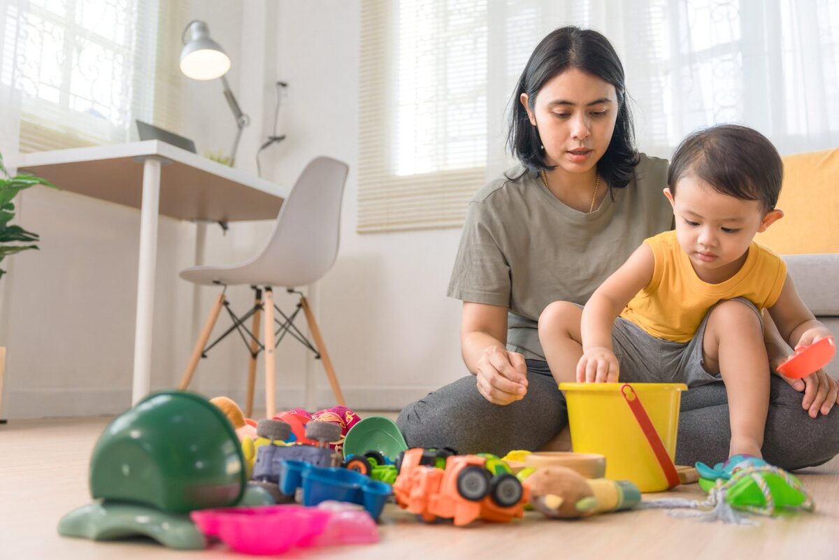 A mother and young child clean up colorful toys in a bright living room together.