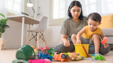 A mother and young child clean up colorful toys in a bright living room together.