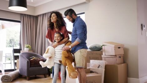 A happy family carrying stuffed animals while moving into a new home, surrounded by boxes and living room furniture.