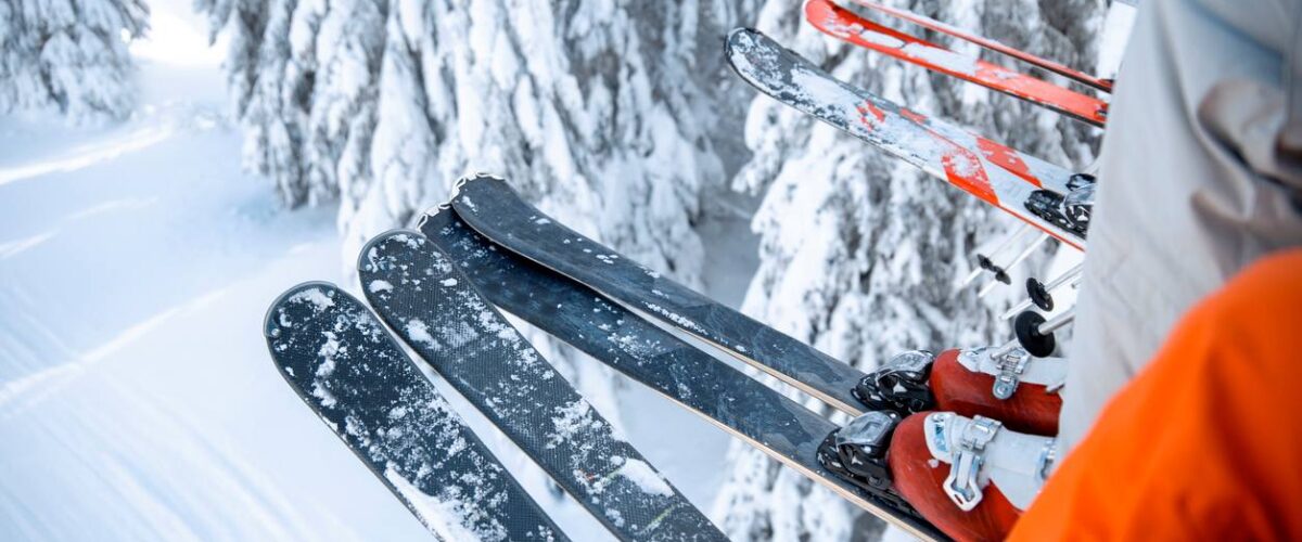 The legs and feet of a group of people on a ski lift above a snowy forest with their skis covered in snow.