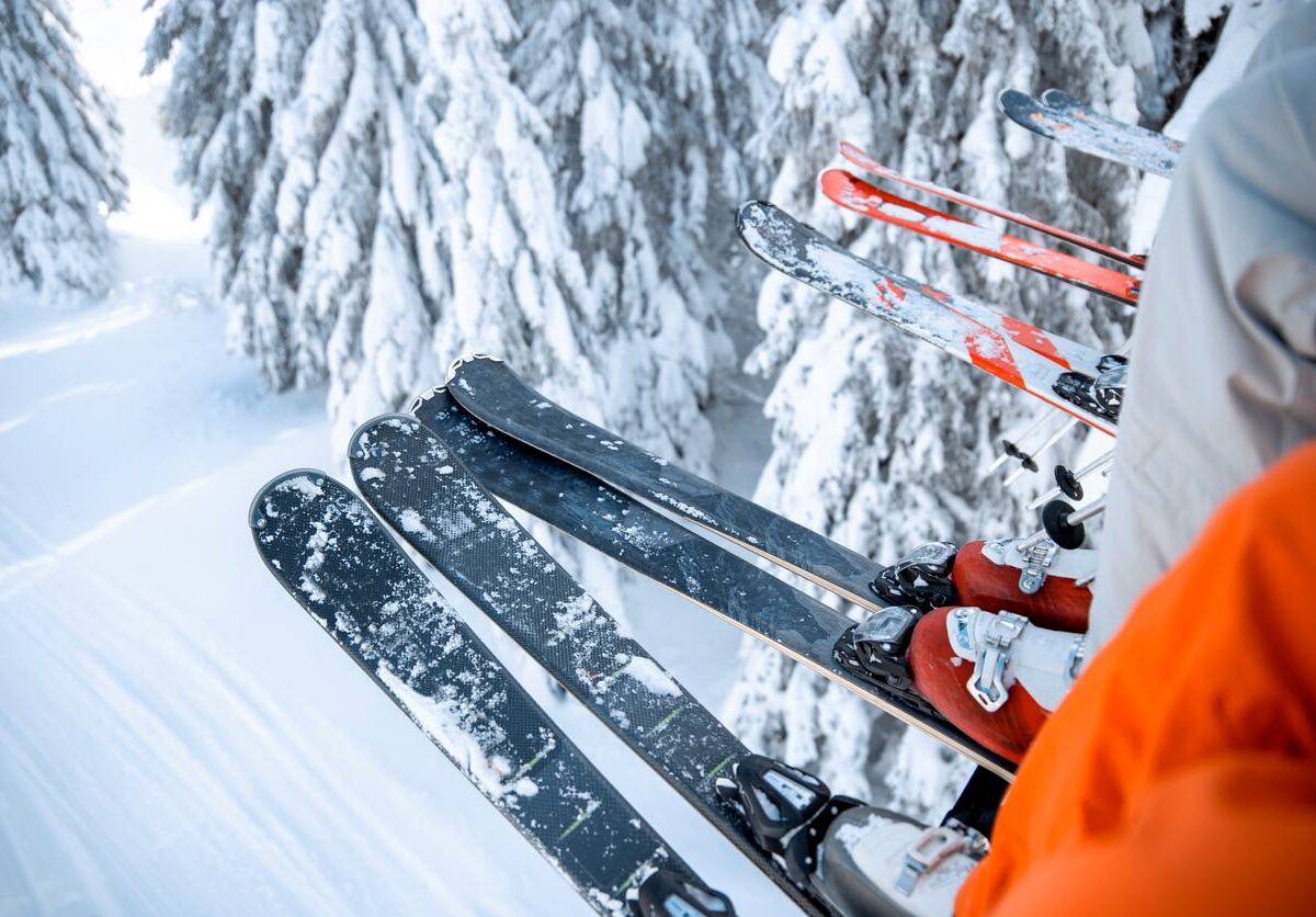 The legs and feet of a group of people on a ski lift above a snowy forest with their skis covered in snow.